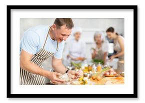 Adult man in apron pours sauce into ready dish at cooking master class