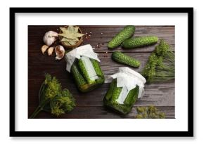 Pickled cucumbers in jars, fresh ones, garlic, dill and dry bay leaves on wooden table, flat lay