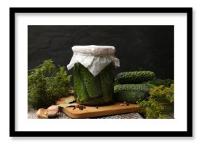 Pickled cucumbers in jar, fresh ones and spices on color wooden table against black background, closeup