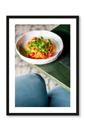Top view of a bowl with noodles, cherry tomatoes, and cilantro on a rustic green table, capturing a vibrant and appetizing vegetarian meal.