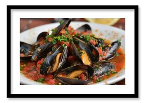 Delicious steamed mussels are served in a rich marinara sauce, garnished with fresh parsley, creating a flavorful seafood dish
