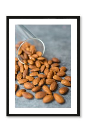 A glass jar spills fresh almonds on a gray stone surface, showcasing their natural texture.
