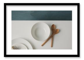 Top view of a clean white table featuring an empty bowl and wooden spoons, kitchen and cooking theme