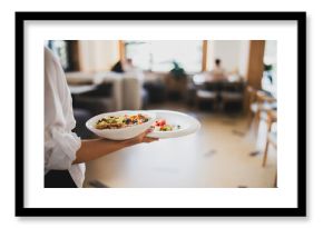 Waiter in white shirt serving two plates with gourmet food and fresh salad in a bright, modern restaurant interior. Selective focus on dishes
