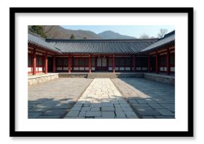 Traditional Korean house courtyard features stone pathways and tiled roofs. Red columns support covered walkways around a central stone patio. Mountains rise in the background under a clear blue sky.