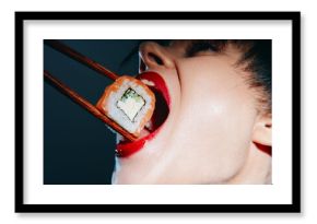 Bold sushi indulgence with vibrant colors and striking lips, highlighting a woman excitedly preparing to eat sushi roll using chopsticks.