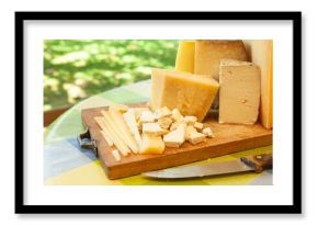 Assortment of sliced and chunked cheeses with knife on wooden cutting board