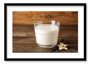 Glass of fresh vanilla milk with sticks and flower on wooden background