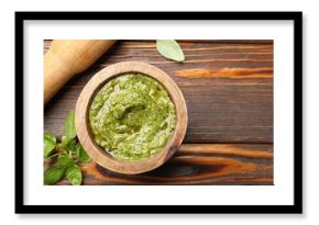 Fresh pesto sauce in mortar, pestle and basil leaves on wooden table, flat lay. Space for text