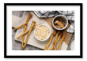 Composition with cutting board, bowls with horseradish sauce and roots on grey grunge background, closeup