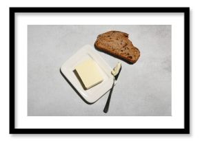 Slice of fresh bread, dish with butter and knife on grey grunge background