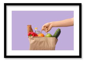Woman holding paper bag with vegetables, fruits, baguette and bottle of oil on purple background