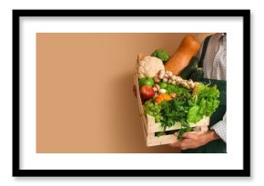Male farmer with box of vegetables and fruits on beige background with space for text, closeup