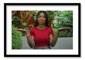 Young woman palms up presenting in a forest park area with green plants and casual red top and jeans  contemplation choice balance.