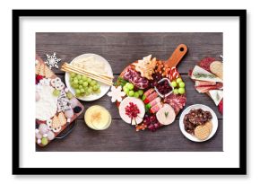Christmas holiday charcuterie table scene on a dark wood banner background. Top down view. Variety of cheese, fruit and meat appetizers.