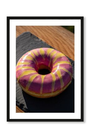 Bright Pink and Yellow Striped Glazed Donut on Black Slate Outdoors