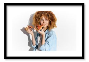 Young woman with curly hair enjoying a slice of pizza, wearing a casual light blue shirt, smiling joyfully, vibrant food photography concept