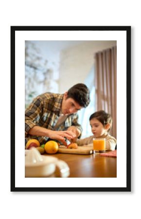 Orange juice glass in bright kitchen scene with lively warm father and little boy moment. Concept of lifestyle storytelling, health visuals, food promotion and positive emotional branding.