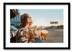 woman fries car sunset beanie sunglasses parking casual enjoying golden hour glow with authenticity and candid lifestyle vibe, mindful living and emotional storytelling in urban roadside scene