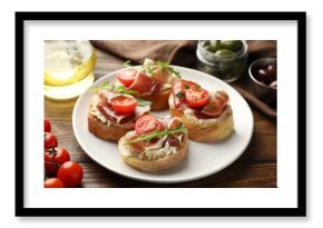 Delicious bruschettas with cream cheese, prosciutto, tomatoes and arugula on wooden table, closeup