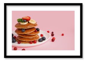 Plate with tasty pancakes, banana slices, cranberries and blueberries on pink background