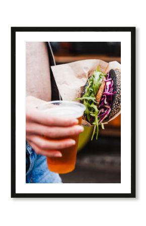Close up of woman hands holding delicious organic salmon vegetarian burger and homebrewed IPA beer on open air beer an burger urban street food festival in Ljubljana, Slovenia