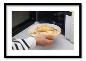Woman putting plate with lunch into microwave indoors, closeup