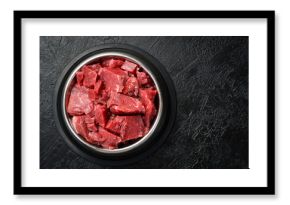 Bowl for a pet with fresh meat. On a black stone background.