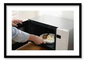 Woman putting plate with food into microwave oven at wooden table indoors, closeup