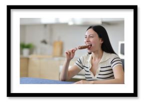 Asian woman biting chocolate ice cream in a kitchen