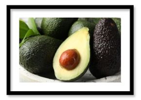 Whole and cut avocados on plate, closeup