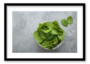 Fresh spinach leaves in a white bowl set on a gray backdrop, showcasing their vibrant green color and healthy appeal, perfect for salads, smoothies, or side dishes. Copy space