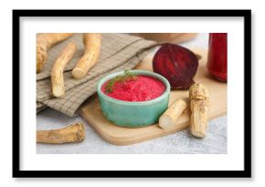 Horseradish sauce with beet in bowl and piece of beet on grey table