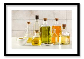 Vegetable fats. Different oils in glass bottles and dishware on white wooden table against tiled wall