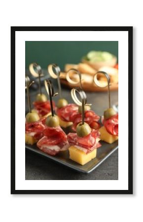 Tasty canapes with olives, prosciutto and cheese on grey table, closeup