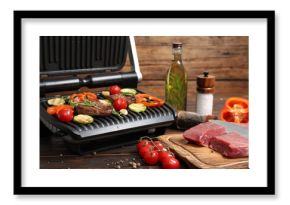 Electric grill with meat, spices and vegetables on wooden table