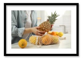 Woman taking pineapple out from string bag at light marble table, closeup
