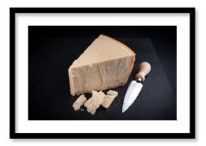 Traditional Parmesan cheese piece with cheese knife during food preparation as close-up on a black design board with text space