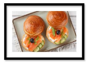 Sandwich with salted salmon, cream cheese, fresh cucumber and olives close-up on a plate on the table. Horizontal top view from above