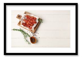 Cutting board with fried bacon rashers, rosemary and bowl of peppercorn on white wooden background