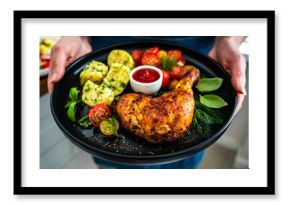 Woman holding plate with roasted chicken leg with boiled potatoes, fresh tomato salad and ketchup 