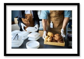 Restaurant staff preparing food orders with hands seen organizing takeaway boxes and serving freshly baked bread on a tray in the kitchen. Workers wearing aprons and gloves