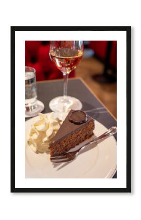 Piece of famous Sachertorte chocolate cake with apricot jam of Austrian origin served with whipped cream in old classic cafe-restaurant in Vienna