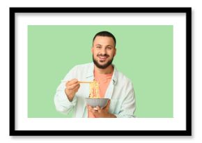 Young man eating tasty ramen on green background