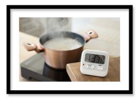 Modern kitchen timer on table against cooking pot in room, closeup