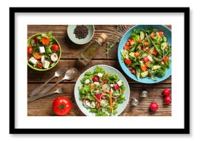 Bowls of fresh vegetable salad with radish and feta cheese on wooden background