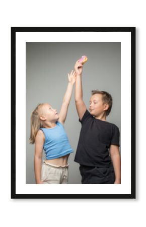 Playful sister and brother having fun holding donuts standing against white wall. Child and chocolate glazed donut