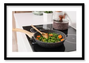 Frying pan with tasty vegetables and spoon on electric stove in kitchen, closeup