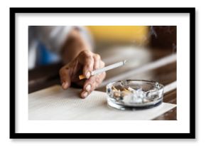 The hand of a smoking woman with a cigarette taps the ash into an ashtray