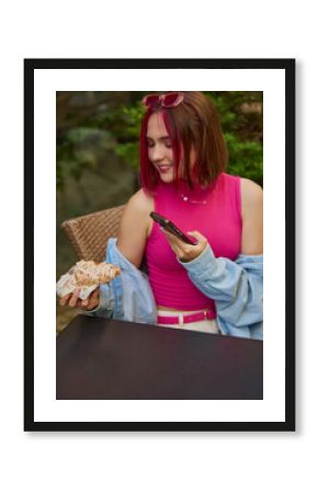 Young woman taking a picture with smartphone of a croissant at an outdoor cafe. Concept of social food culture, Gen Z dining, influencer marketing, casual lifestyle branding.